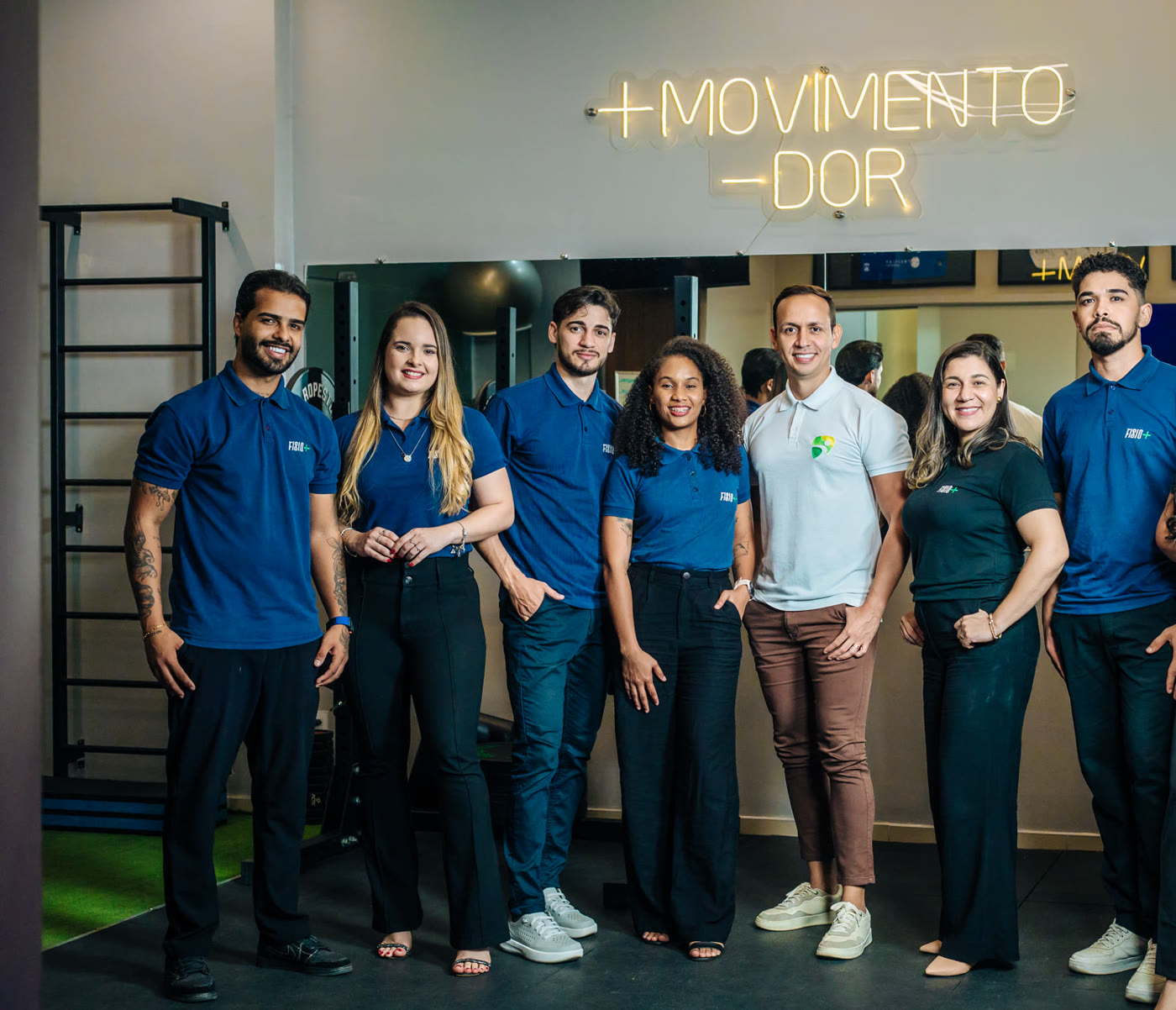 Dr. William Paixão e a equipe Fisio+ reunidos sob o letreiro +MOVIMENTO -DOR, na clínica